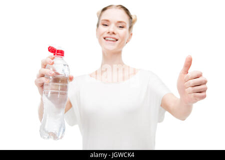 Sorridente ragazza tenendo la bottiglia con acqua e mostrando il pollice in alto isolato su bianco Foto Stock