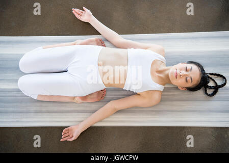 Al di sopra di vista della giovane donna asiatica facendo eroe reclinabili pongono (Supta Virasana) sul materassino yoga Foto Stock