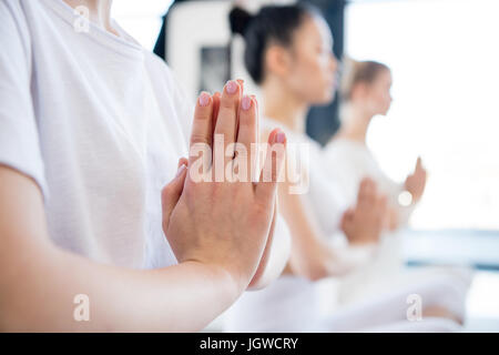 Concentrato di giovani donne meditando in lotus posano con Namaste mudra gesto in ambienti interni Foto Stock