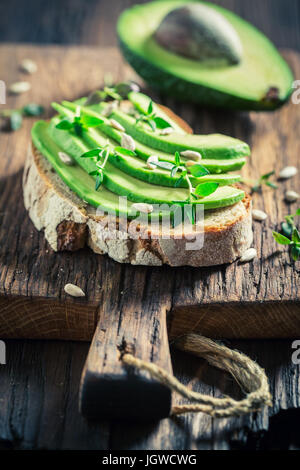 Sandwich con avocado, erbe e semi sul tavolo di legno Foto Stock