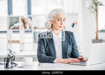 Ritratto di fiducioso imprenditrice digitando su laptop al lavoro in ufficio moderno Foto Stock