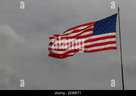 Bandiera degli Stati Uniti d'America o a stelle e strisce al vento, contro un grigio cielo nuvoloso, estratte a sinistra, copia spazio, su un palo. Foto Stock