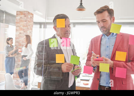 Vista attraverso il vetro di colleghi il brainstorming utilizzando sticky notes Foto Stock