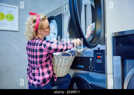 Donna rimozione servizio lavanderia dal asciugatrice in lavanderia a gettoni Foto Stock