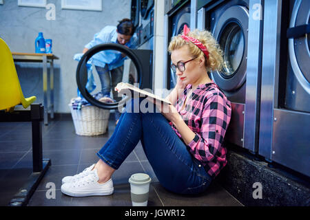 Donna seduta sul pavimento lavanderia libro di lettura Foto Stock