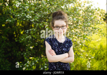 Ritratto di una ragazza che indossa occhiali in campo con la fioritura degli alberi Foto Stock