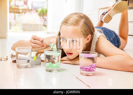 Ragazza distesa sul pavimento facendo esperimento con bicchieri di acqua Foto Stock