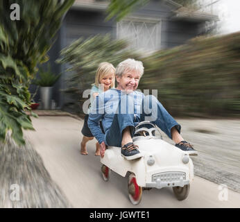 Nipote spingendo la nonna sul suo giocattolo auto Foto Stock