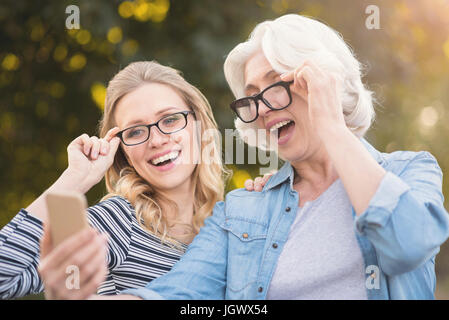 Tenersi in contatto con i nostri seguaci. A sostegno di età compresa elegante nonna a piedi nel parco pur esprimendo felicità e tenendo selfie con giovani daug Foto Stock