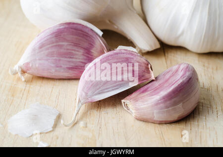 Vista ravvicinata della rosa tre spicchi di aglio, con tutta le lampadine non sgusciati in background. Bucce di cartaceo sono sparsi su un graffiato in legno bo di trinciatura Foto Stock