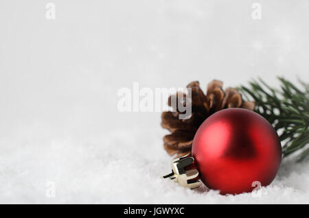 Un Natale di confine e con sfondo rosso ninnolo, fir cono e ramo verde, immerso nel bianco della neve falsa nell'angolo inferiore destro. Stelle scintillanti in b Foto Stock