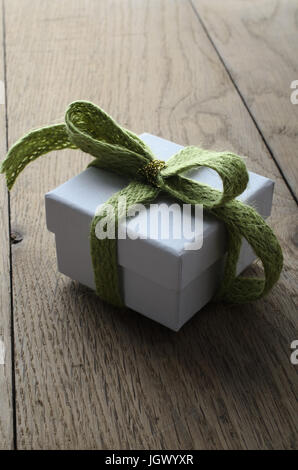 Leggermente alzato di un bianco, piazza lidded confezione regalo su una vecchia quercia tabella planked, legato ad un arco con un delicato verde wooly nastro di tessuto e wrappe Foto Stock