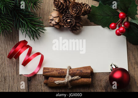 Scatto dall'alto di un messaggio vuoto card sul tavolo in legno di quercia, confina con una miscela di coni di naturale e cannella, artificiale holly e foglie di pino rosso e ba Foto Stock