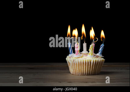 Un compleanno cupcake in un semplice caso di carta con sette strisce, candele accese su una tavola di legno con sfondo nero.