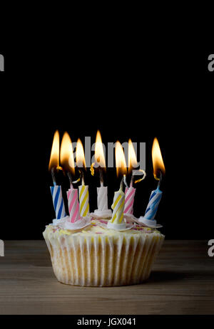 Un compleanno cupcake in un semplice caso di carta con sette strisce, candele accese su una tavola di legno con sfondo nero.