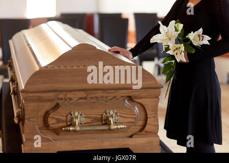 Donna con fiori di giglio e bara al funerale Foto Stock