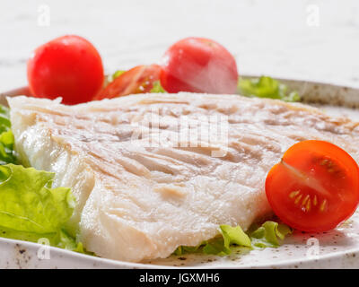 Vista ravvicinata del caldo il baccalà alla griglia con basilico e pomodori ciliegia nel quartiere alla moda di piastra bianca. Foto Stock