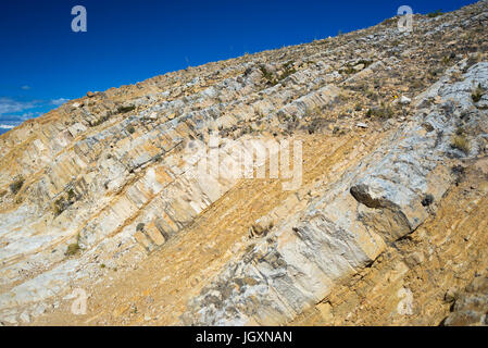 Close up di antiche rocce sedimentarie stratificate sperone di roccia, piegata dal potere di geologici movimento crostale. Cielo blu chiaro. Foto Stock