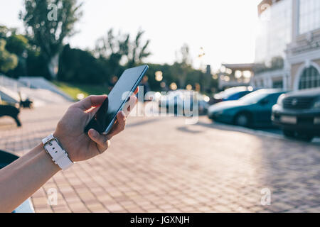 Telefono cellulare nella donna la mano contro città estate sfondo, close-up Foto Stock