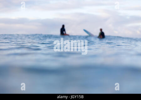 Due fuori fuoco surfers sedersi nella distanza sulle loro tavole da surf in attesa per un'onda a comparire all'orizzonte. Foto Stock