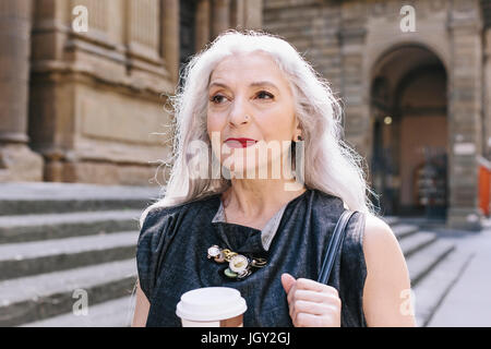 Donna matura con lunghi capelli grigi con caffè sulla strada di Firenze, Italia Foto Stock