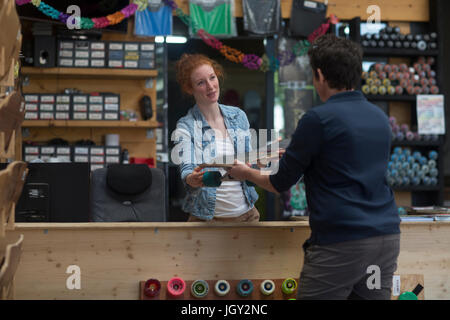 Donna che lavorano nel negozio di skateboard, tramandando skateboard al cliente Foto Stock