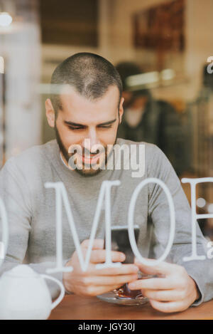 Giovane uomo seduto in cafe, utilizza lo smartphone, vista attraverso la finestra Foto Stock