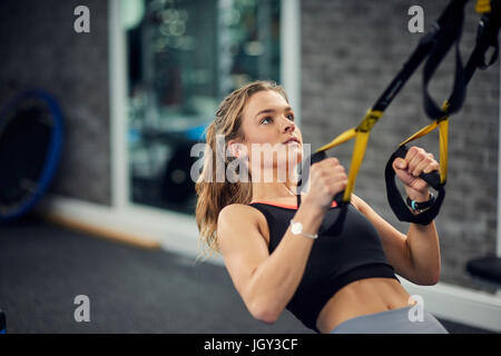 Giovane donna facendo tirare ups sulle maniglie di esercizio in palestra Foto Stock