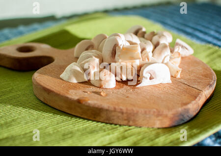 Il processo di taglio di funghi champignon su un tagliere di legno sul tessuto verde sullo sfondo di close-up Foto Stock