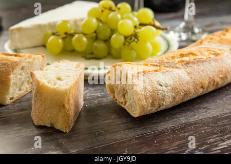 Pane francese, una fetta di formaggio brie e uva su una scheda. Foto Stock