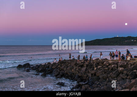 La gente guarda il sole e la luna piena ascesa al Byron Bay, Nuovo Galles del Sud, Australia. Foto Stock