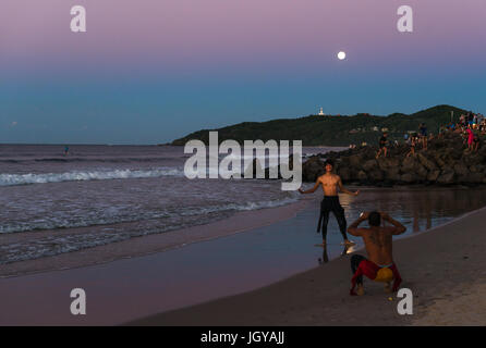 La gente guarda il sole e la luna piena ascesa al Byron Bay, Nuovo Galles del Sud, Australia. Foto Stock