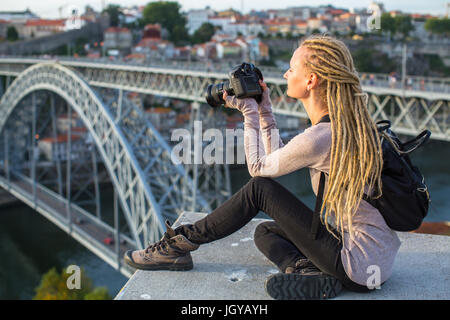 Giovane donna turistica con fotocamera seduto sulla piattaforma di osservazione di fronte al Dom Luis I ponte che attraversa il fiume Douro a Porto, Portogallo. Foto Stock