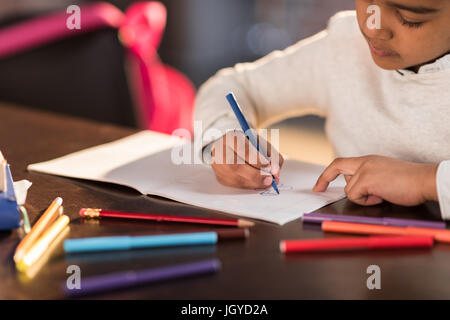 Ritagliato colpo di incantevole piccola ragazza seduta a tavola e disegno con pennarello, svolgendo compiti concept Foto Stock
