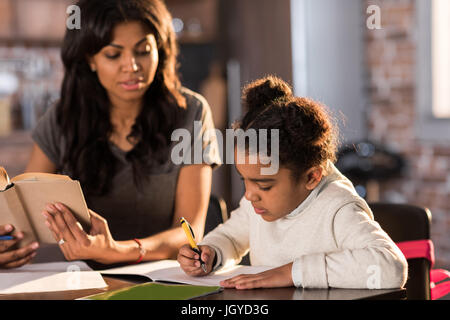 Madre guardando carino piccola figlia a fare i compiti a casa, compiti help concept Foto Stock