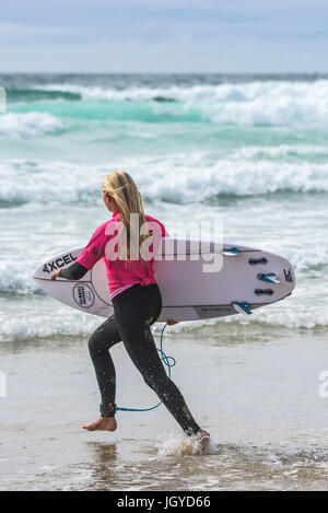 Navigare in UK. Una giovane donna surfer in esecuzione nel mare come lei compete nel Regno Unito scuole surf campionato. Nerf scontro di Groms a Fistral nel nuovo Foto Stock