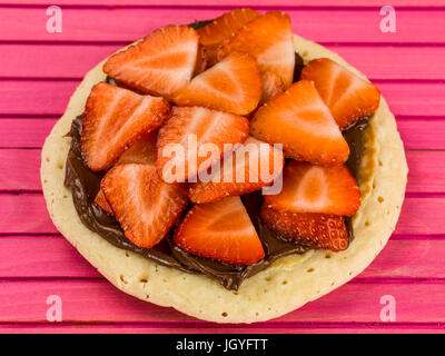 Pancake con fragole e cioccolato da spalmare contro un sfondo rosa Foto Stock