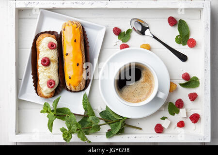 Bere caffè con eclairs nel vassoio in legno Foto Stock