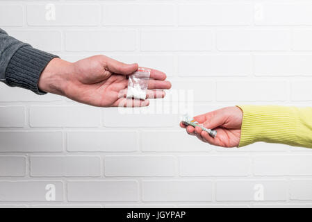 Trasferimento di denaro e la droga close-up contro un bianco muro di mattoni Foto Stock