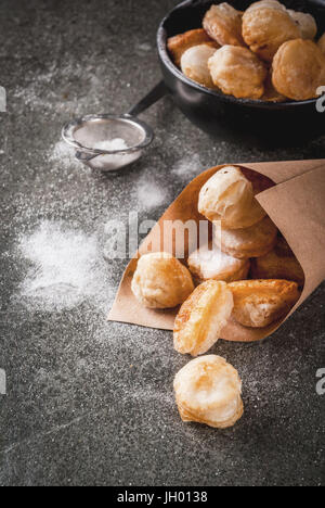 In casa la cottura, sfogliatine. Cibo alla moda. Cronuts popcorn, puff ciambelle fori in una ciotola nero e un sacco di carta, con zucchero a velo. Su una pietra scura Foto Stock