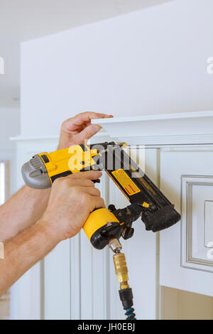 Carpenter brad mediante pistola sparachiodi alla corona di stampaggio su mobili da cucina il framing trim, con l'etichetta di avvertimento che tutti gli strumenti di potere avere su di loro mostrato illus Foto Stock