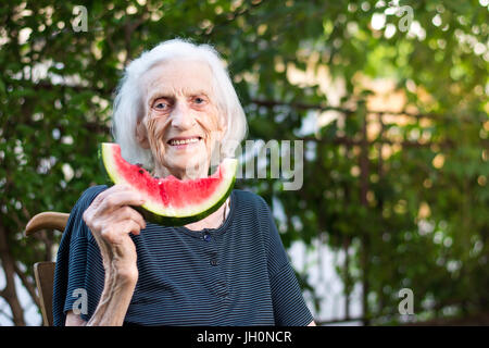 Allegra donna senior azienda fetta di anguria nel cortile posteriore Foto Stock