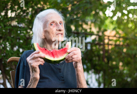 Senior donna azienda fetta di anguria nel cortile posteriore Foto Stock