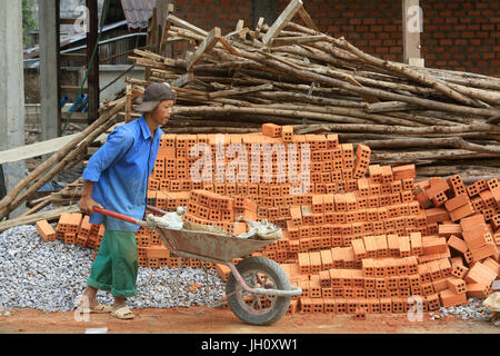 Uomo che porta i mattoni in una carriola. Sito in costruzione. Laos. Foto Stock