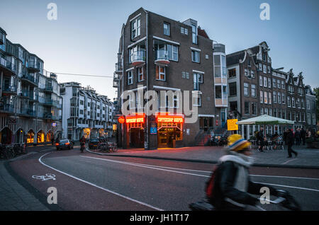 Amsterdam, Paesi Bassi - 25 April, 2017: Corse per adulti una bicicletta nella parte storica di Amsterdam con tipiche case tradizionali contro la caffetteria Foto Stock