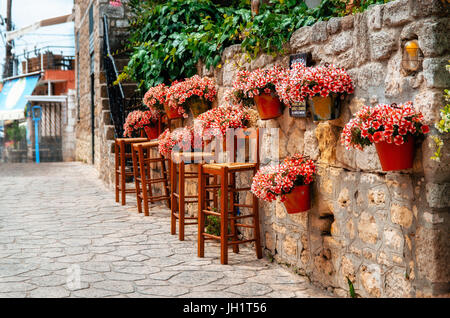 Vasi di fiori di colore rosso su una parete di pietra in piena fioritura con barstools intorno al cafe, Afitos, Halkidiki, Grecia Foto Stock