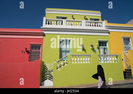 Stagliano donna coperta in veste nera passa case vivacemente colorate in Bo-Kaap, il malese e zona musulmana, Città del Capo Foto Stock