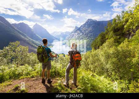 Due escursionisti a viewpoint in montagna godendo di una splendida vista della valle con un lago e soleggiata clima caldo in estate, verdi alberi intorno Foto Stock