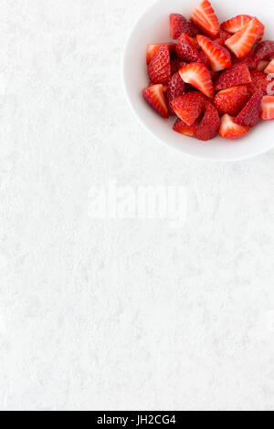 Tagliare le fragole in un colore bianco porcellana ciotola isolato su marmo bianco lo sfondo con un sacco di spazio copia. Foto Stock