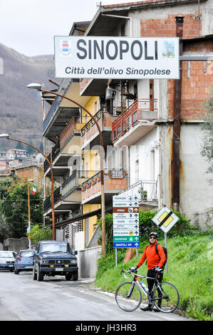 Una touring ciclista in piedi con la sua bicicletta sul lato di una strada all'entrata della città di Sinopoli, Calabria, Italia. Foto Stock